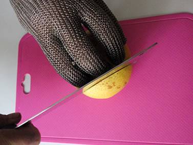 A hand wearing chainmail glove is cutting a pear on the pink board.