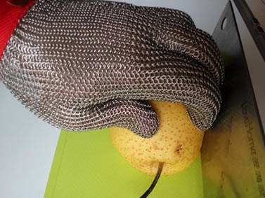 The side view of a hand wearing chainmail glove is cutting pear on the yellow board.