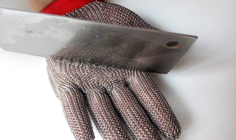 A hand wearing chainmail glove is cutting by a kitchen knife.